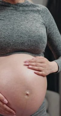 Hamile kadın kulaklık takıyor ve karnına dokunuyor. Hamilelik boyunca müzik ve rahatlamanın keyfini çıkarıyor.