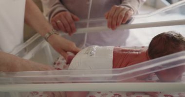 Yumuşak eller yeni doğmuş bir bebeği rahatlatıyor beşikte yatıyor, bakımı ve yeni hayatı sembolize ediyor