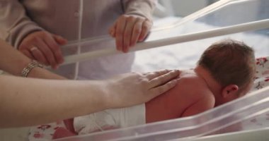 Yeni doğan bebek beşikte dinleniyor. Anne ve babası yakınlarda şefkatini ve şefkatini gösteriyor.