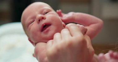 Açık ağızlı ve mavi gözlü küçük bir bebek yetişkin ellerince nazikçe tutulurken duygularını ifade eder.