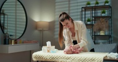 Anne, iyi aydınlatılmış bir kreş odasında, yumuşak bir soyunma odasında, yeni doğmuş bebek bezini nazikçe değiştiriyor. Anne Altını Değiştiren Bebek Bezi