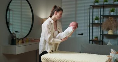 Anne sevgiyle yeni doğmuş bebeğini hafif ışıklı bir çocuk odasında tutarak, hassas bir bağ ve bakım anı yaratıyor. Anne kucağında yeni doğan bebek