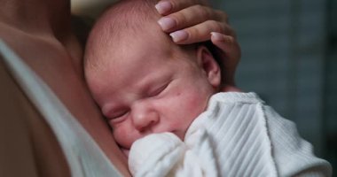 Sevgi dolu kollarla güven içinde uyuyan barışçıl bir bebeğin yakın çekimi. Yeni doğmuş Bebek Huzur içinde Uyuyor