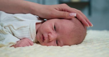 Nazik eller, yumuşak desenli battaniyeye uzanmış bebek başını okşar, erken çocukluğun hassas anlarını yakalar. Yeni doğmuş Bebek Huzur içinde Uyuyor