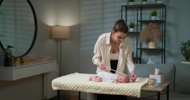 Anne, yeni doğan bebeklerinin uzunluklarını rahat bir bebek odasındaki soyunma masasında dikkatlice ölçer. Anne Yeni Doğan Bebek Boyunu Ölçüyor