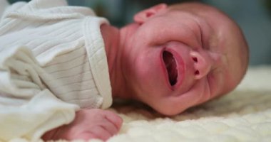 Yeni doğmuş barışçıl bir bebeğin, çizgili tuluma sarılı yumuşak bir battaniyenin üzerinde mışıl mışıl uyuduğu yakın plan. Nazik anne, uyuyan bebeğinin alnını yumuşak bir battaniyeyle öper.