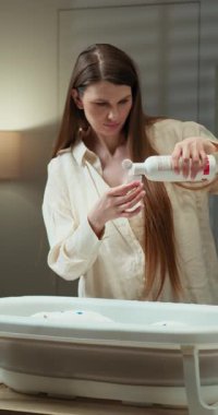 Anne banyo için hazırlanan portatif bebek küvetine sıvıyı dikkatlice döker.