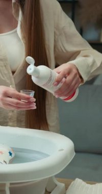 Bakıcı su ısısını test etmek için yıldız desenli bebek yastığıyla birlikte katlanabilir havzanın üzerinde küçük bir bardak kullanarak banyo ve güvenlik kontrolü yapar.