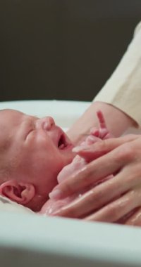 Ebeveyn, ağlayan yeni doğmuş bebeği küvette yıkar. Sıkıntılı bebek yüzüne ve küçük ellerine yakın plan çeker.
