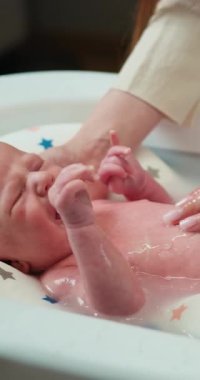 Sıkıntılı yeni doğmuş bir bebek, elleri nazikçe vücudunu tutan küçük bir küvette yıkanırken yüksek sesle ağlar.