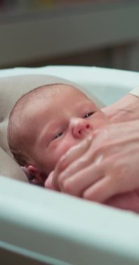 Yeni doğmuş bir bebeğin cildinde su damlacıkları ve nazikçe onu destekleyen bir eliyle küvette yıkanması.