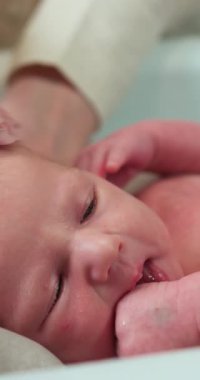 Yeni doğmuş bir bebeğin yüzünün banyo sırasında yumuşak köpükler ve suyla nazikçe yıkandığı yakın plan.