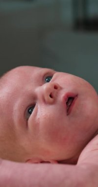 Yeni doğmuş bebek yüzlü mavi gözlü yumuşak battaniyeden yukarı bakan, yüzüne yakın minik elli