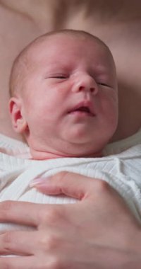 Yeni doğmuş bebek yüzünün yakın plan profili mavi gözlü ve hassas ciltli, anne-baba eli tarafından nazikçe tutulan