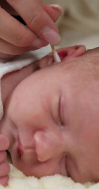 Ebeveyn nazikçe yeni doğmuş bebeklerin kulaklarını pamuklu çubukla temizler. Narin cilt ve yumuşak yüz hatlarını gösterir.