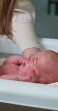 Annelerin ellerinin yakın çekimi yeni doğmuş bebeğinin yüzüne ve başına banyo sırasında nazikçe masaj yapıyor.