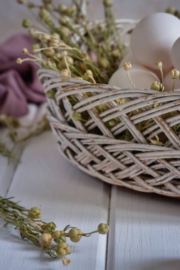 Fresh white eggs in a basket with dried flowers on a white wooden table