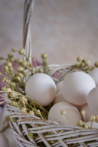 Fresh white eggs in a basket with dried flowers on a white wooden table