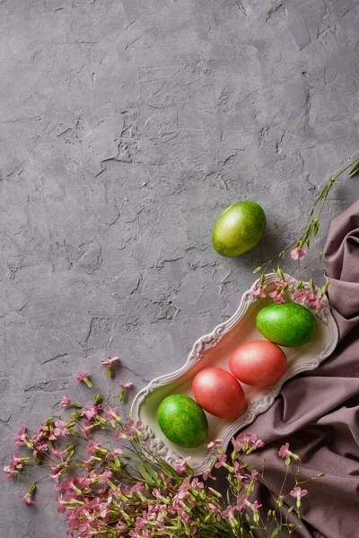 Painted easter eggs with pink wildflowers on gray concrete background close-up