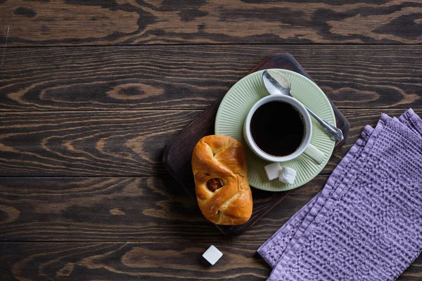 Eski ahşap masanın üzerinde taze çörek ve kurutulmuş kayısı ile sade kahve.