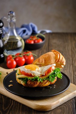 Lezzetli ve yararlı bir kahvaltı. Çırpılmış yumurtalı, domatesli, peynirli ve yeşillikli sandviç. Tahta bir masada, siyah bir tabakta.