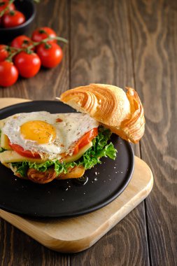 Lezzetli ve yararlı bir kahvaltı. Çırpılmış yumurtalı, domatesli, peynirli ve yeşillikli sandviç. Tahta bir masada, siyah bir tabakta.
