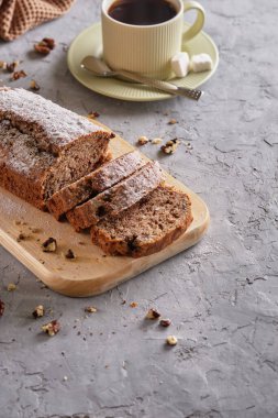 Lezzetli ve aromalı muzlu kek, fındıklı ve çikolatalı tahta tahta tahta üzerinde, arka planda bir fincan kahveyle yakın plan.