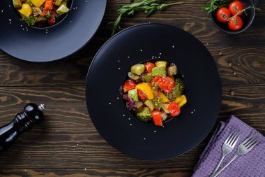 Lezzetli ve yararlı yiyecekler. Eski ahşap masadaki yuvarlak siyah tabakta ızgara sebzeler.