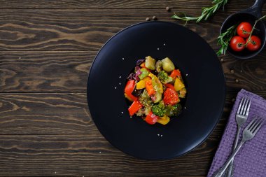 Lezzetli ve yararlı yiyecekler. Eski ahşap masadaki yuvarlak siyah tabakta ızgara sebzeler.