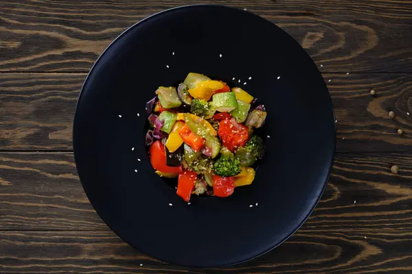 Lezzetli ve yararlı yiyecekler. Eski ahşap masadaki yuvarlak siyah tabakta ızgara sebzeler.