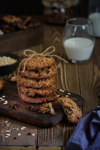 Lezzetli ve lezzetli yulaf ezmeli kurabiyeler fındıklı, kuru üzümlü ve baharatlı eski ahşap masa üzerinde bir fincan sütle.
