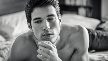 Tişörtsüz seksi erkek model yatağında tek başına yatıyor.