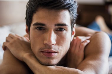 Tişörtsüz seksi erkek model yatağında tek başına yatıyor.