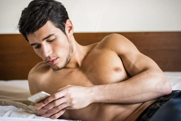 Beau jeune homme au lit tapant sur son téléphone portable — Photo