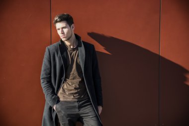 Kırmızı Duvara yaslanan Kış Giysisi Giyen Genç Adam