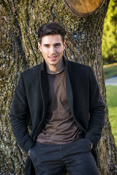 Handsome young man leaning against tree — Stock Photo, Image