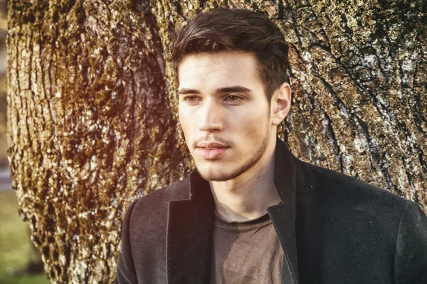 Joven guapo apoyado en un árbol — Foto de Stock