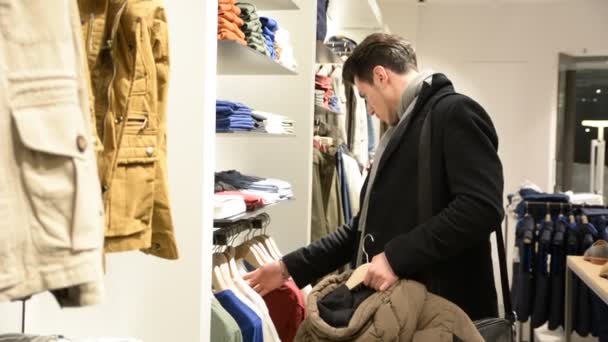 Jonge man voor het kiezen van kleding in de winkel — Stockvideo