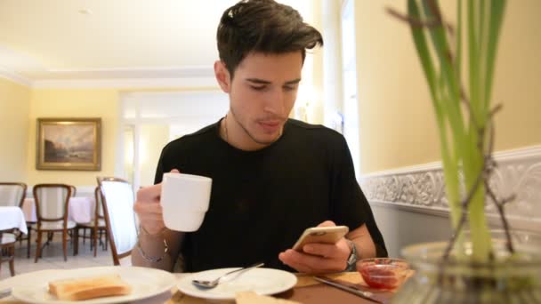 Junger Mann trinkt Kaffee, während er auf das Telefon schaut — Stockvideo