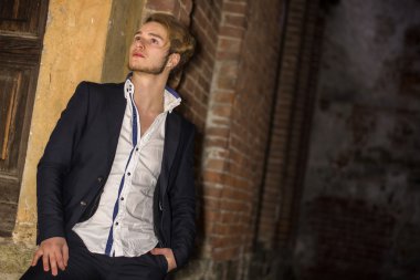 Yakışıklı delikanlı tuğladan duvara yaslanmış.