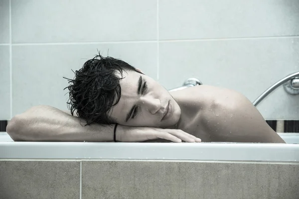 Schöner junger Mann in der Badewanne zu Hause mit Bad — Stockfoto