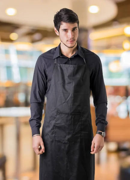 Young chef or waiter wearing black apron in restaurant — Stok Foto