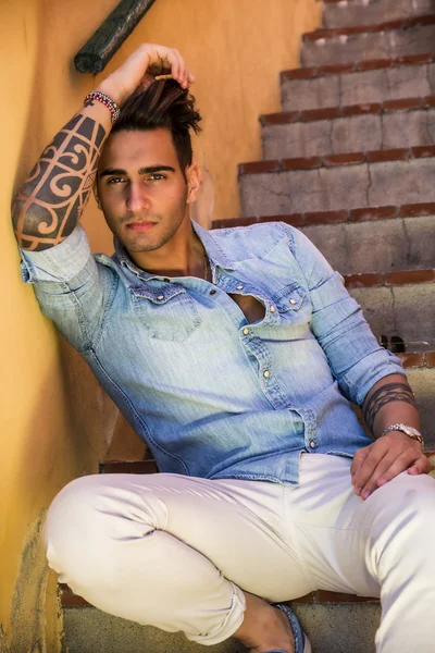 Handsome man sitting on stairs while looking at camera — Stock Photo, Image