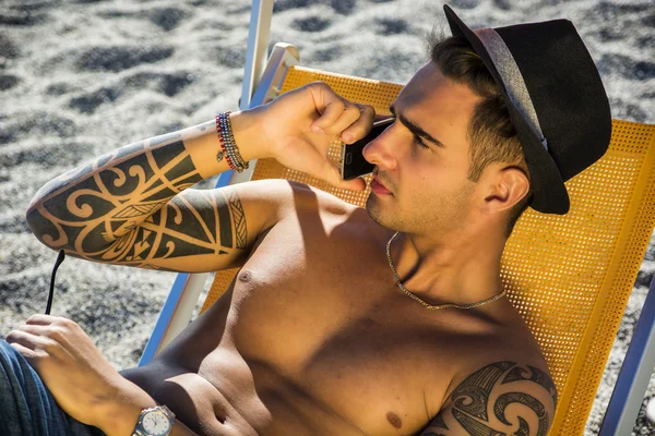 Young man on deckchair at beach talking on phone — Stock Photo, Image