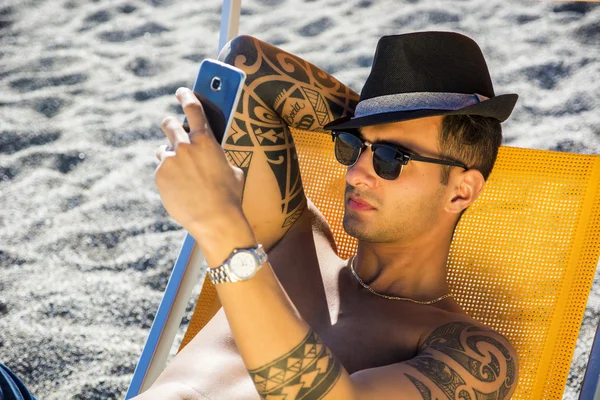 Young man lying on deckchair at beach — Stock Photo, Image