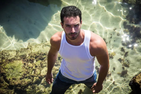 Atlético homem no mar ou oceano por rochas, wet t-shirt — Fotografia de Stock