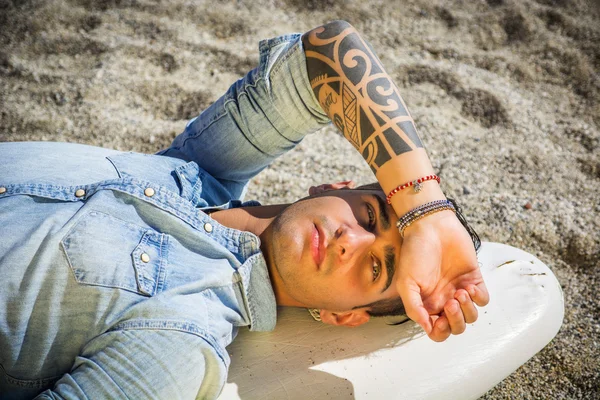 Красивый мужчина лежал на доску для серфинга на пляже — стоковое фото