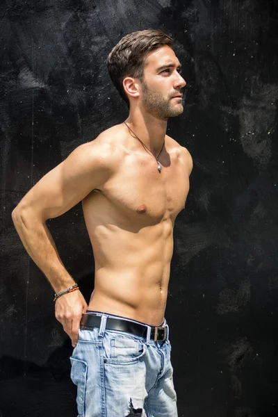 Handsome bearded shirtless young man standing against black wall — Stock Photo, Image