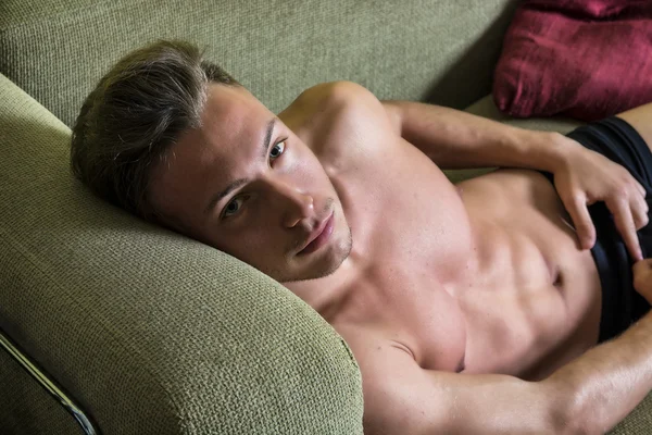 Без рубашки мышечной молодого человека у себя дома на диване — стоковое фото