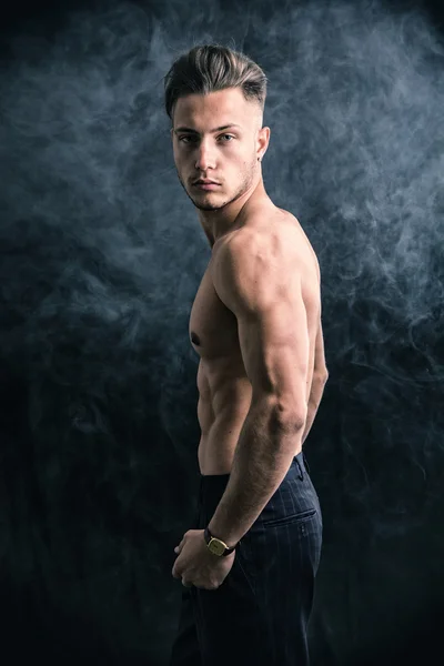 Schlanke sportliche shirtless junger Mann stehend auf dunklem Hintergrund — Stockfoto